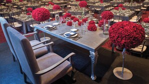 Un salón de banquetes con mesas redondas dispuestas para cenar, cada una con centros de mesa florales rojos y cubiertos.