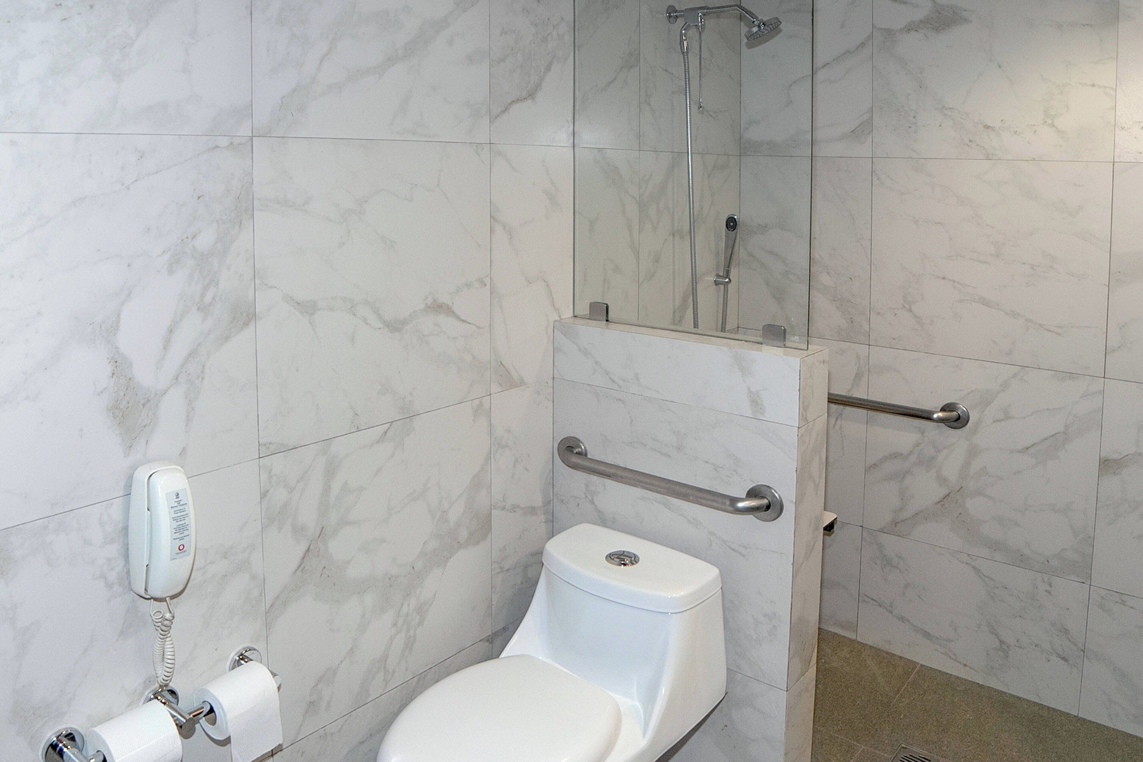 Une salle de bain équipée de toilettes, d’un sèche-mains, d’un miroir et d’un espace douche.
