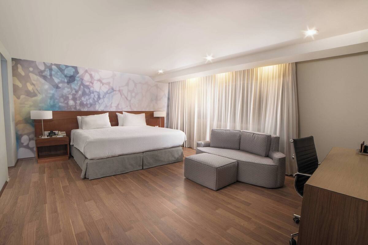 Una habitación de hotel moderna con una cama grande, un sofá, un escritorio y una mesita de noche.