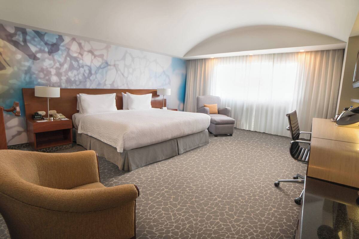 Habitación de hotel con una cama grande, un escritorio, una silla y una mesita.
