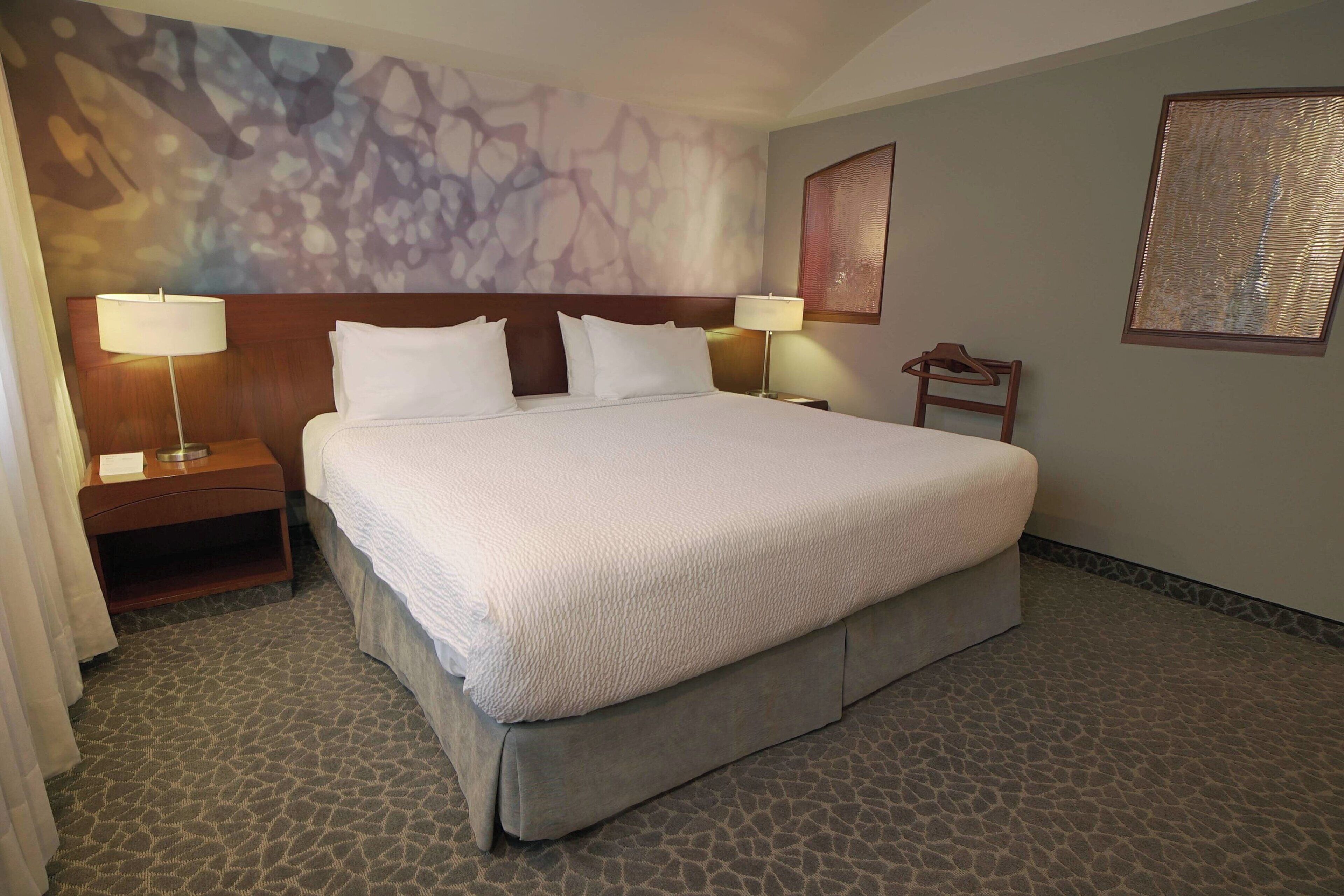 Habitación de hotel con una cama grande, dos mesitas de noche con lámparas, un cabecero y una pared decorada con arte abstracto.