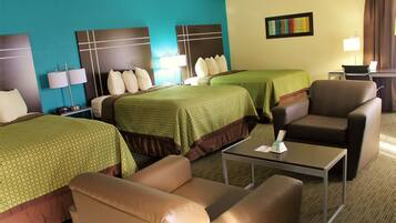 A hotel room with two beds, a sofa, a chair, a small table, and a desk with a lamp.