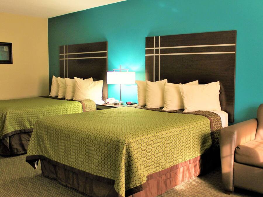 A hotel room with two single beds, a chair, a nightstand with a lamp, and a framed picture on the wall.