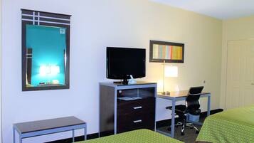 Quarto de hotel com escrivaninha, televisão, poltrona, cama e espelho.