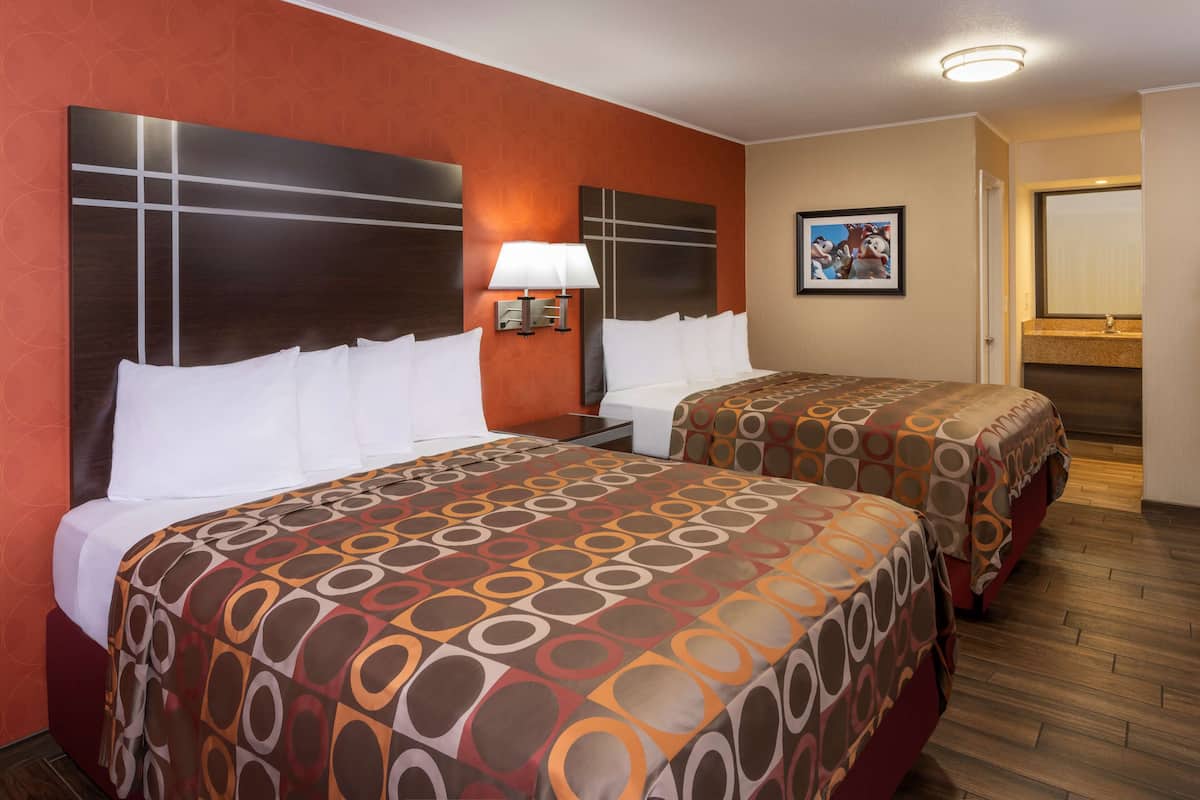 Une chambre d’hôtel avec deux lits, une table de chevet, une lampe fixée au mur et un tableau encadré.