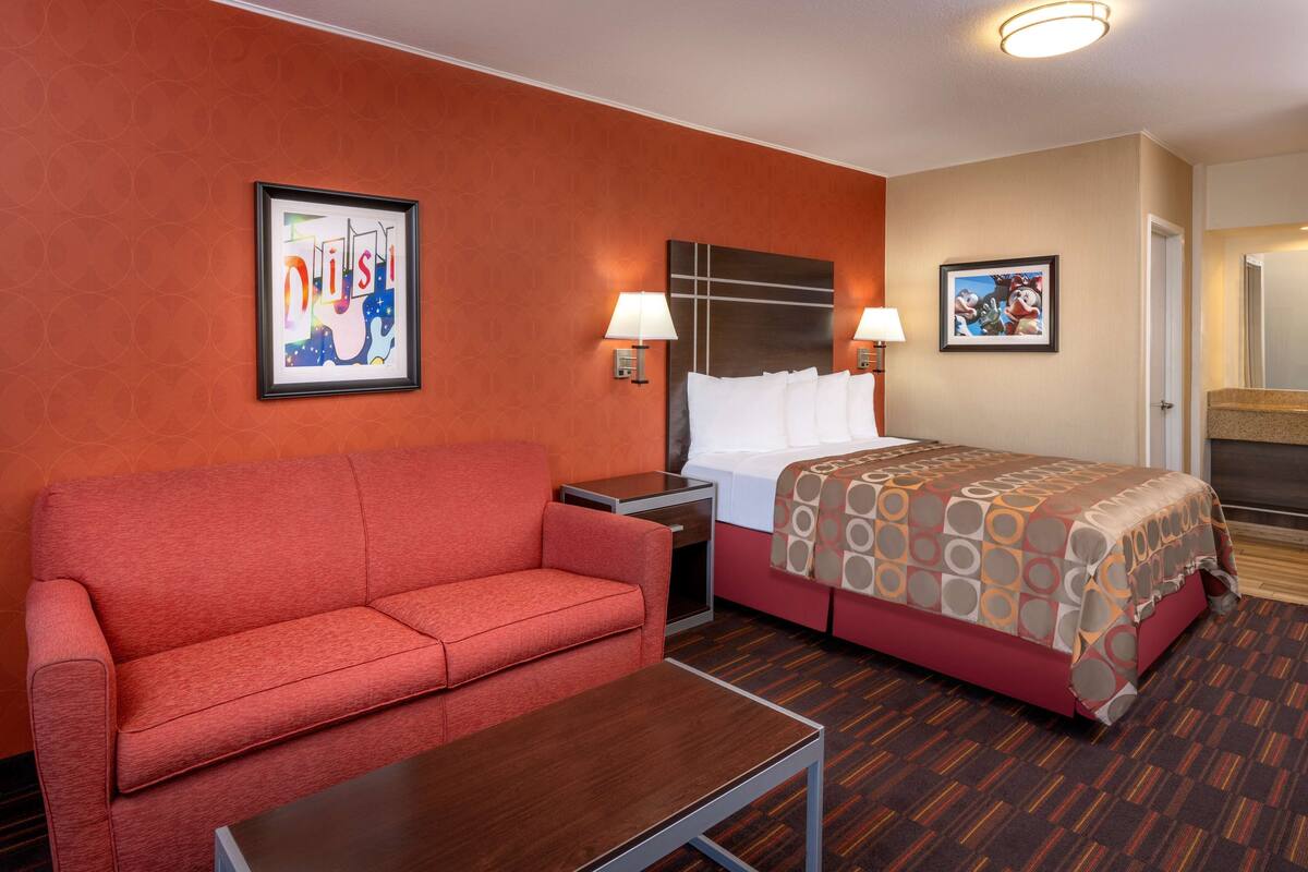 Une chambre d’hôtel avec un canapé rouge, un lit recouvert d’une couvre-lit à motifs, deux tables de chevet avec des lampes et des œuvres d’art accrochées aux murs.