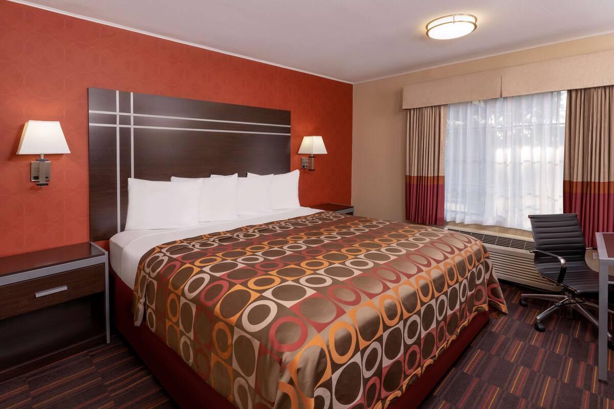 Une chambre d’hôtel avec un grand lit, deux tables de chevet avec des lampes, un bureau avec une chaise et une fenêtre avec des rideaux.