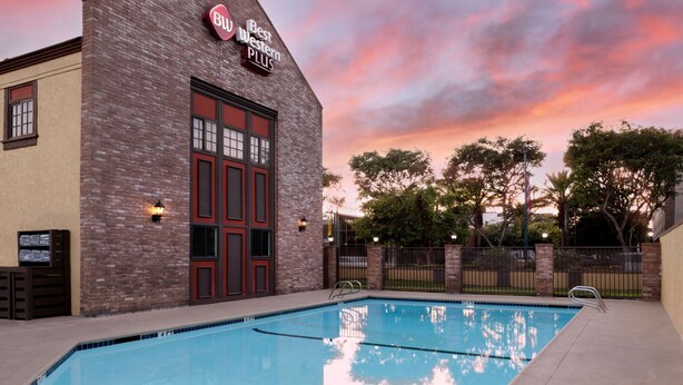 A pool area with a brick building labeled "Best Western Plus" and a sunset sky. - Best Western Plus Raffles Inn & Suites (Anaheim)