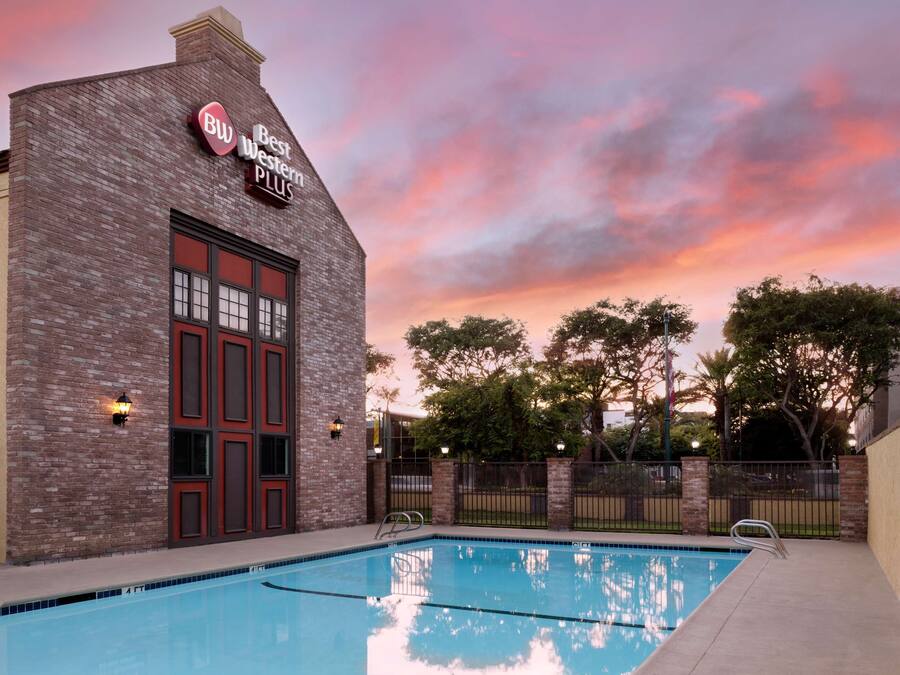 Uma área de piscina com um edifício de tijolos identificado como "Best Western Plus" e um céu ao pôr do sol.