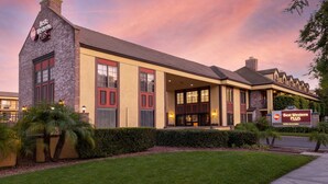 A Best Western Plus hotel with a brick facade, large windows, and a well-maintained lawn. - Best Western Plus Raffles Inn & Suites (Anaheim)