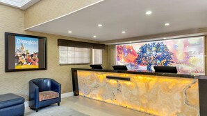 A reception area with a marble counter, a framed Disneyland poster, a blue armchair, and a colorful abstract artwork. - Best Western Plus Raffles Inn & Suites (Anaheim)