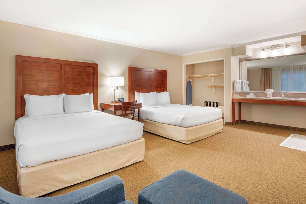 A hotel room with two beds, a desk, a chair, a bathroom with a mirror, and a carpeted floor.
