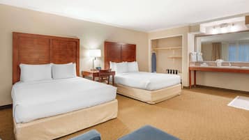 Quarto de hotel com duas camas, uma escrivaninha, uma cadeira, banheiro com espelho e piso coberto por carpete.