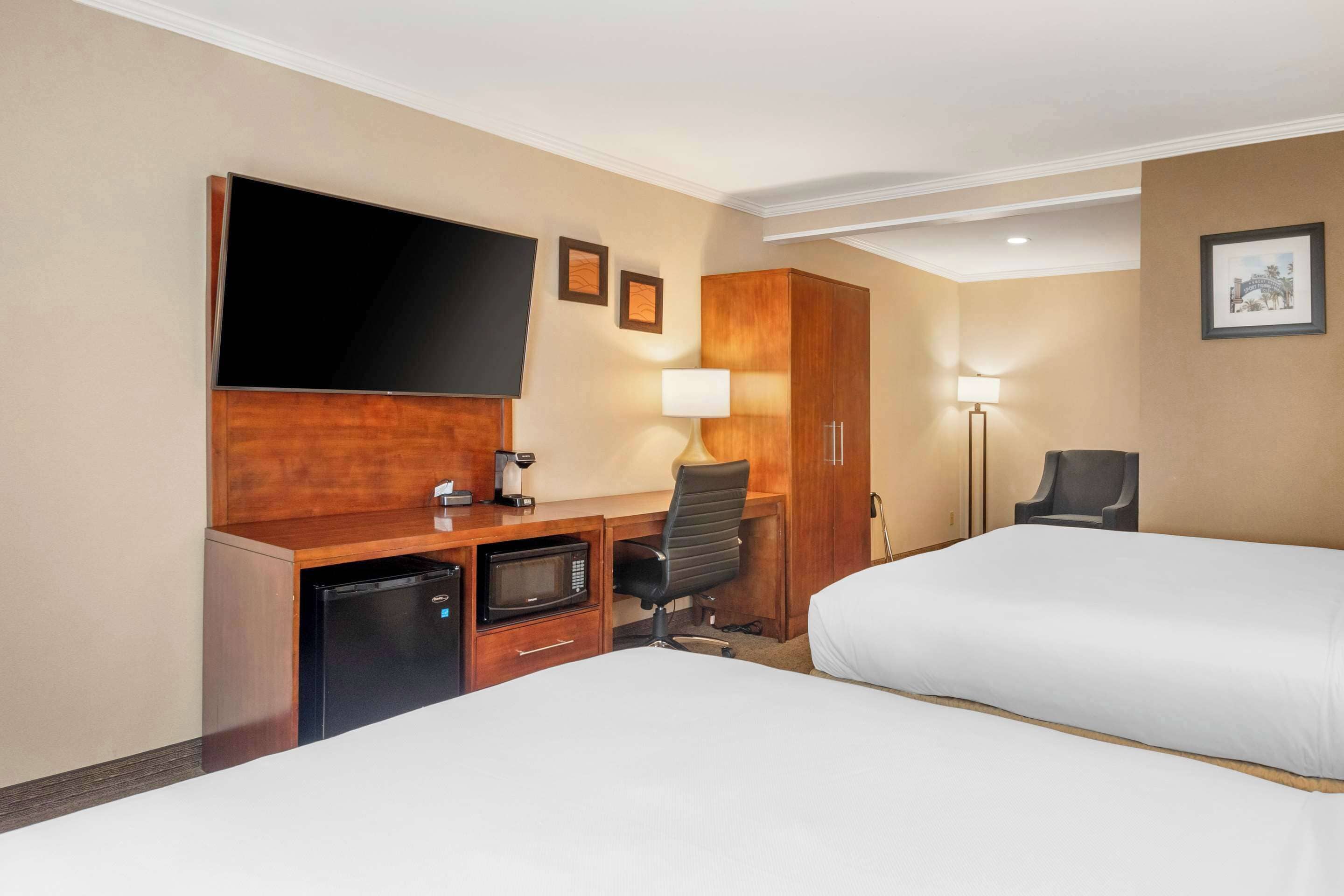 Een hotelkamer met twee bedden, een bureau met een flatscreen televisie, een magnetron, een koffiezetapparaat en een stoel.