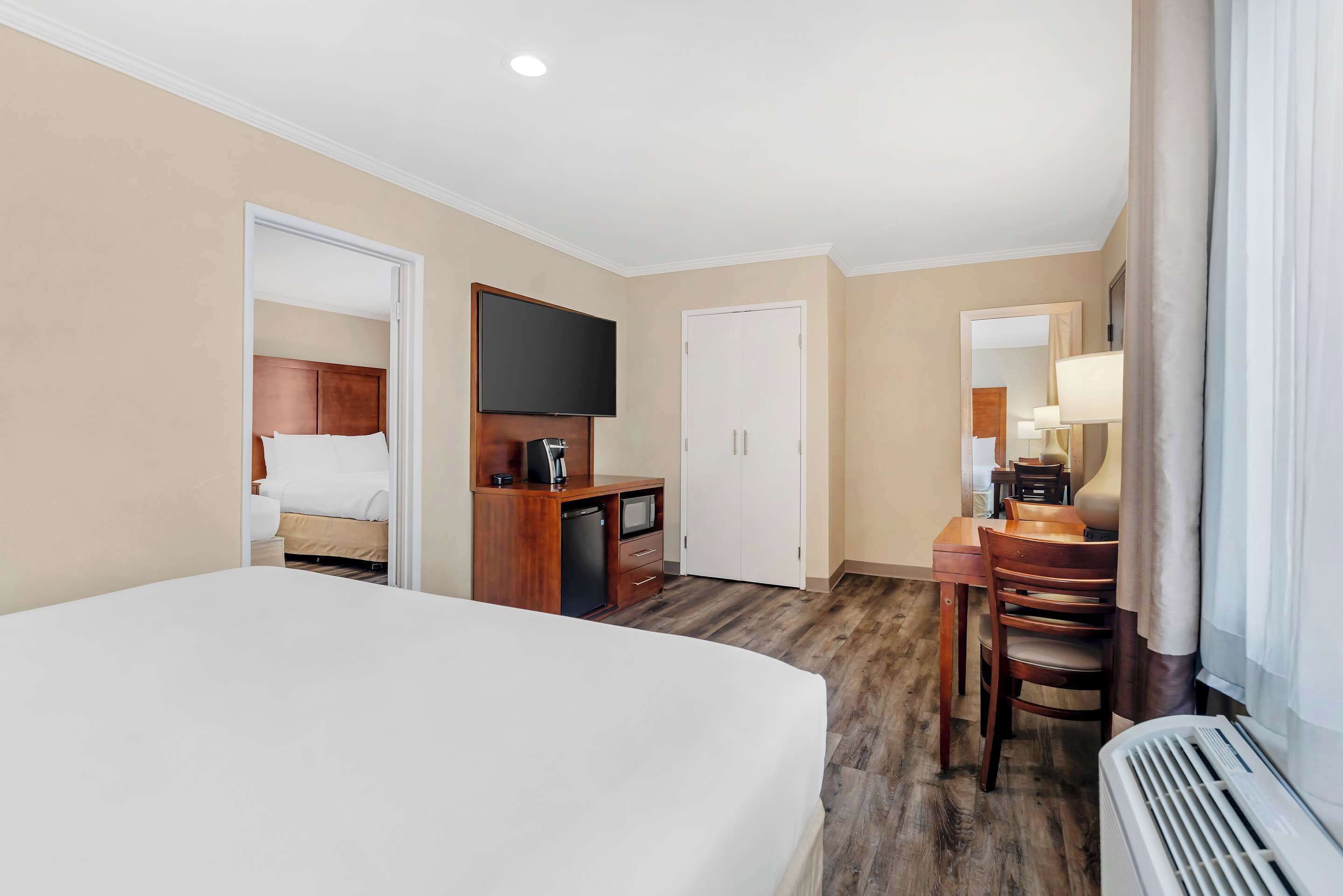 Habitación de hotel con una cama grande, un escritorio con silla, televisión, armario y ventana con cortinas.