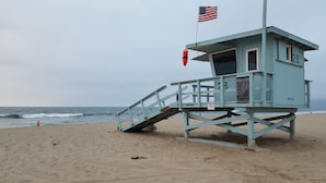 Una torre de salvavidas con una bandera, un flotador y datos de contacto de emergencia en la playa.