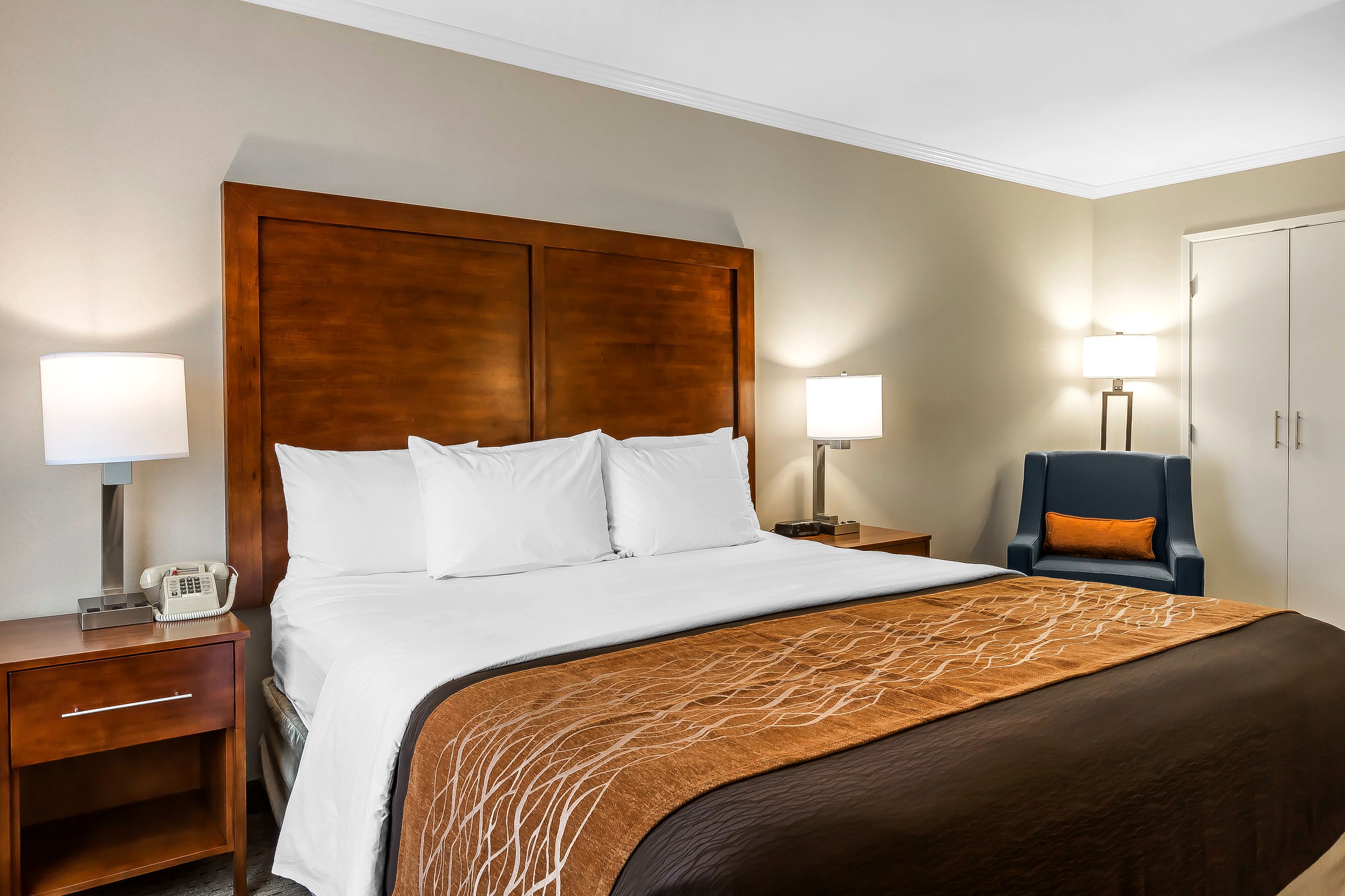 Habitación de hotel con una cama grande, dos mesitas de noche, una silla y un armario.