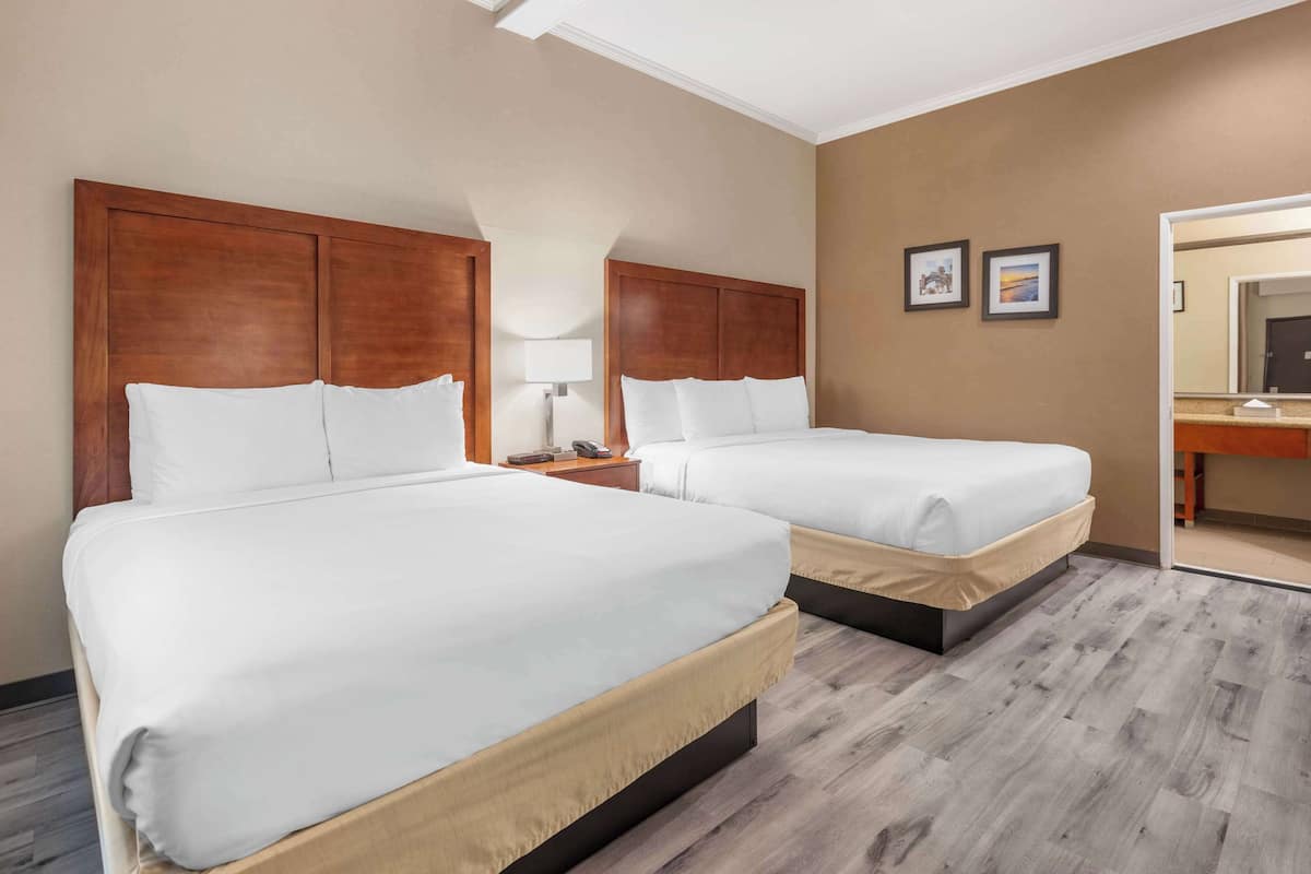 A hotel room with two beds, a nightstand, a lamp, and a mirror.