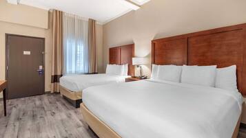 A hotel room with two beds, a wooden headboard, a desk, and a window with curtains.