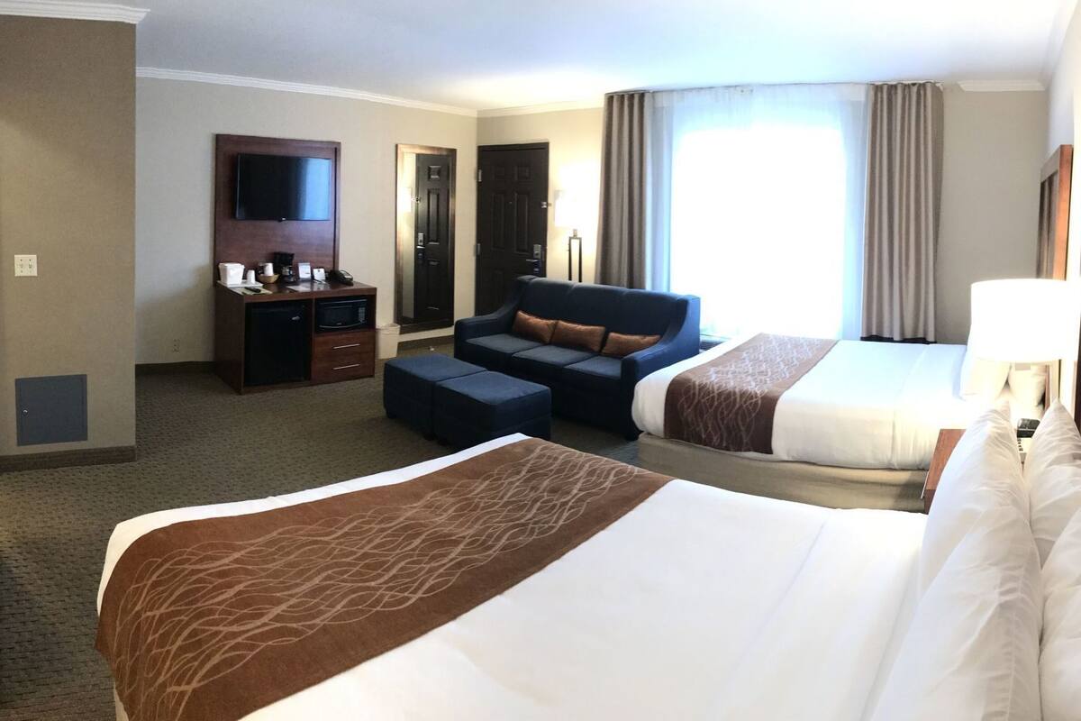 A hotel room with a large bed, a sofa, a desk with a TV, and a window with curtains.