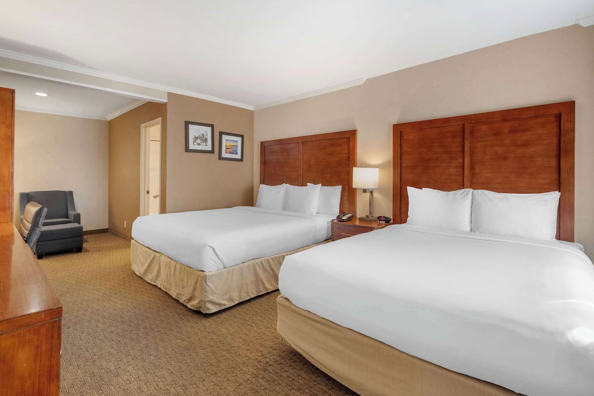 A hotel room with two beds, a desk, a chair, and a lamp.