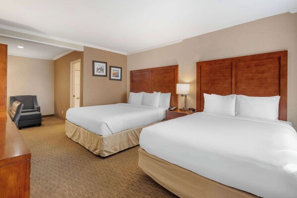 A hotel room with two beds, a desk, a chair, and a lamp.