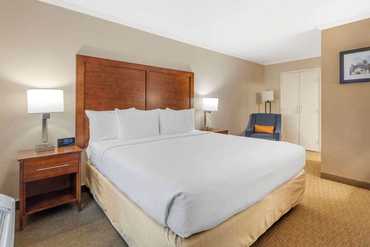 A hotel room with a large bed, two bedside tables with lamps, a chair, and a wardrobe.