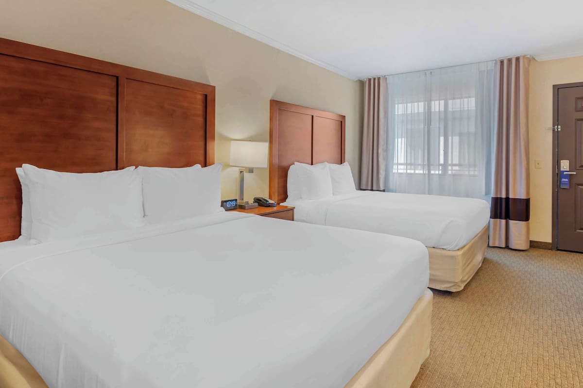 A hotel room with two beds, a wooden headboard, a nightstand with a lamp, and a door with a security lock.