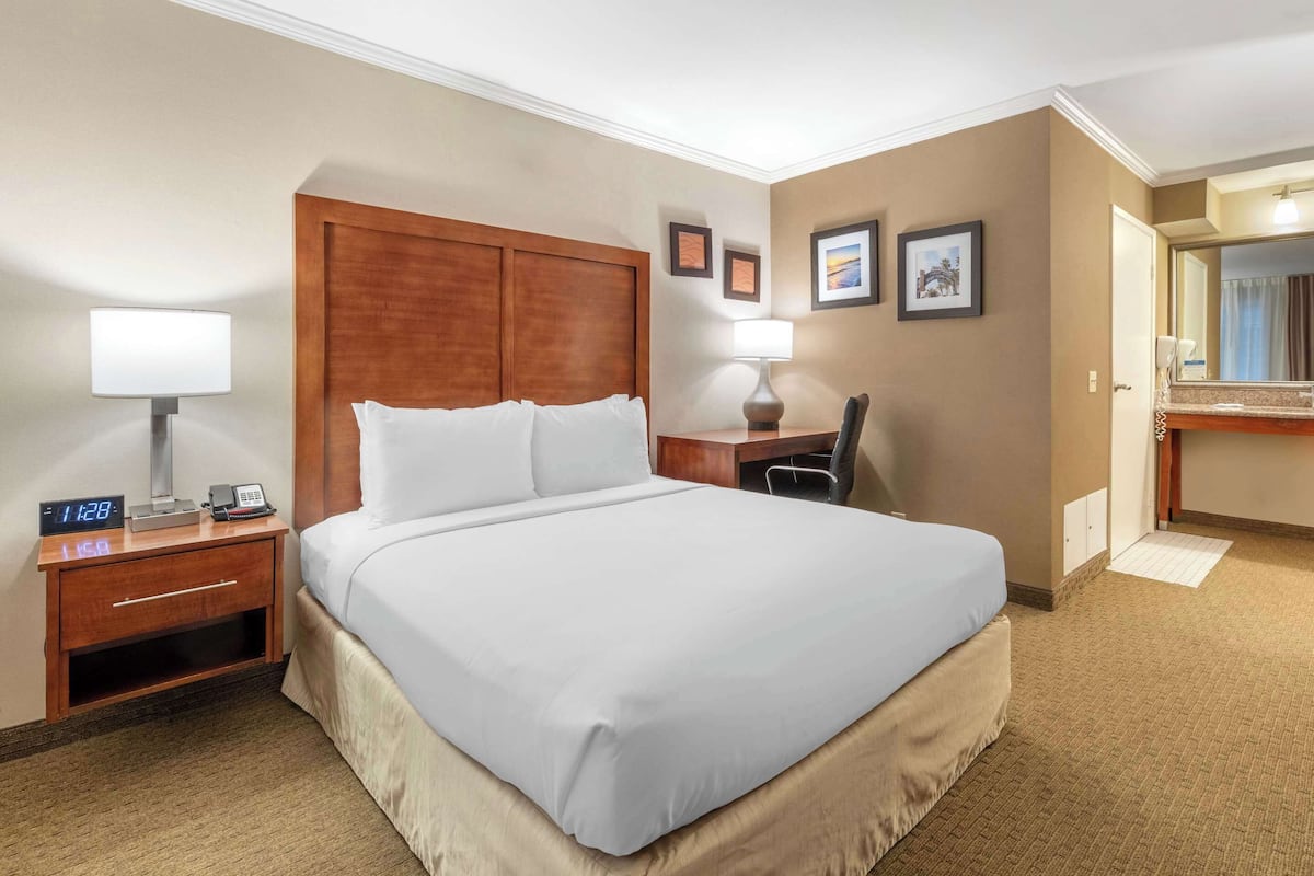A hotel room with a large bed, bedside tables, a desk with a chair, a mirror, and framed pictures on the wall.
