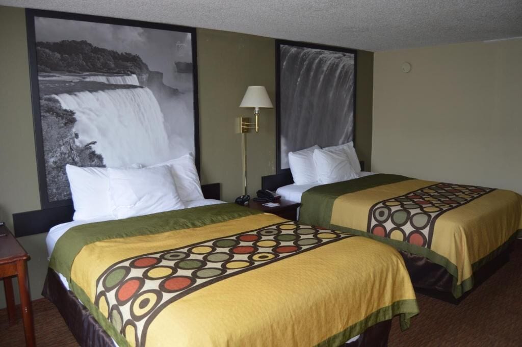 Habitación de hotel con dos camas, una mesita de noche, una lámpara y un cuadro grande de una cascada en la pared.