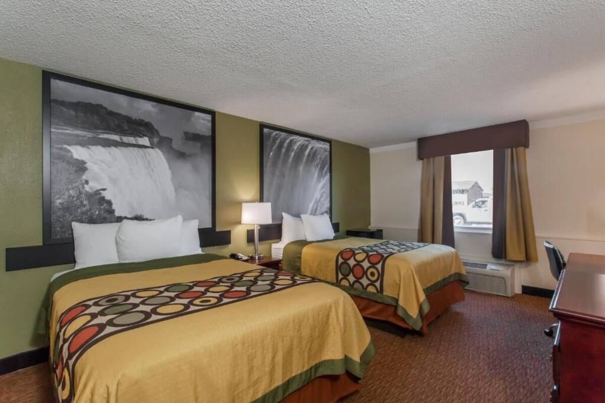A hotel room with two beds, a large wall-mounted TV, a desk, and a window with curtains.