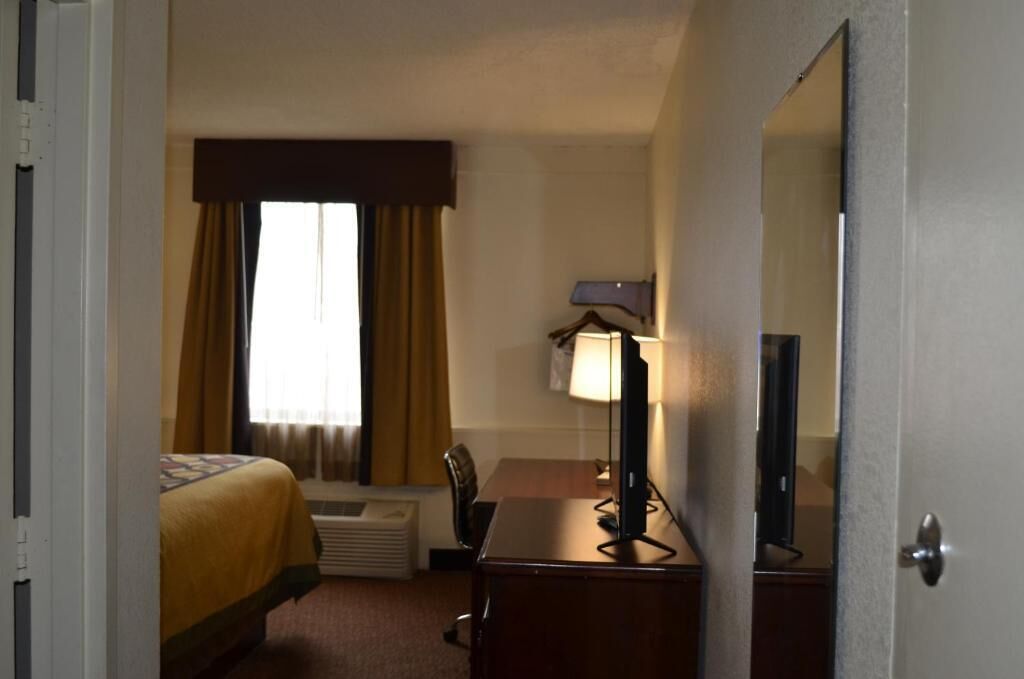 A hotel room with a bed, a desk, a lamp, a television, and a window with curtains.