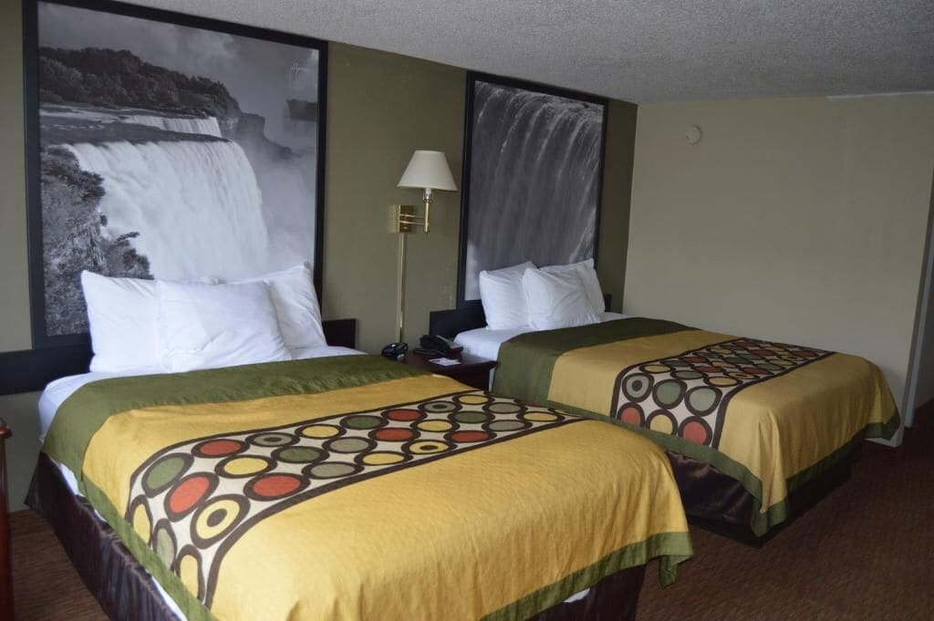 Een hotelkamer met twee bedden, elk voorzien van een beddekleed met dessin, een nachtkastje, een lamp en een groot schilderij van een waterval aan de muur.