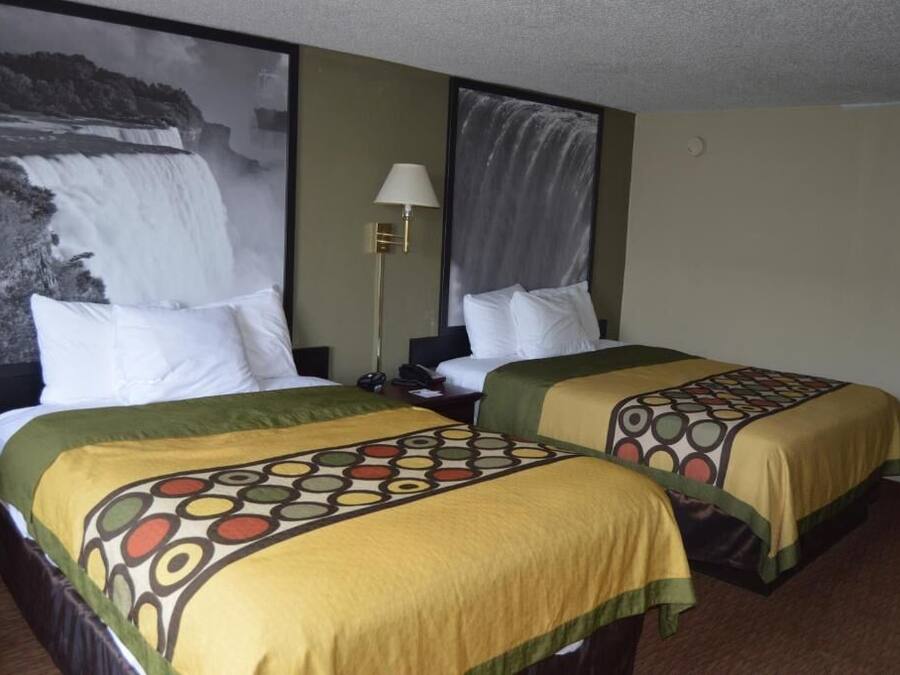 Een hotelkamer met twee bedden, elk voorzien van een beddekleed met dessin, een nachtkastje, een lamp en een groot schilderij van een waterval aan de muur.