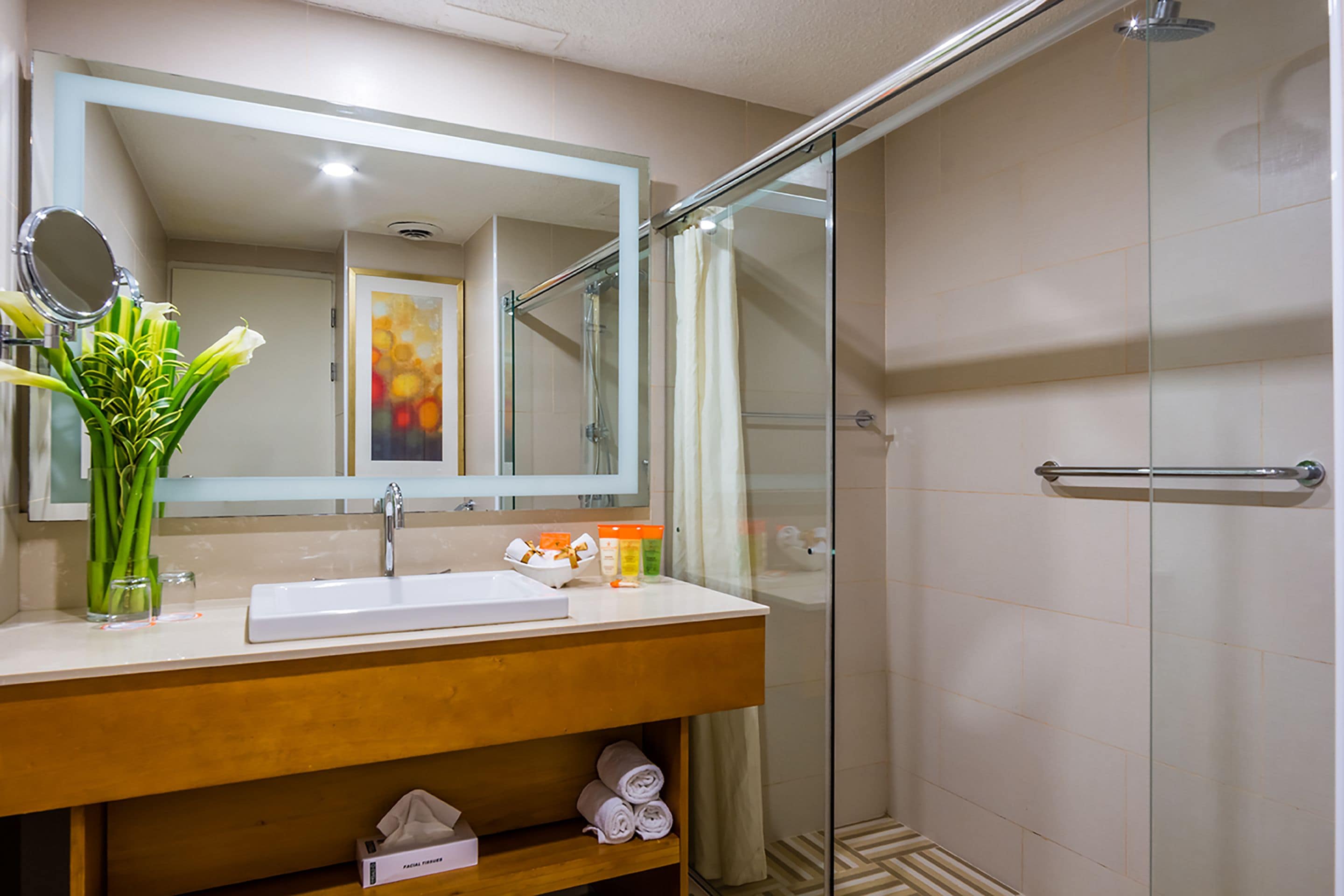 Een badkamer met een douchecabine van glas, een wastafel met spiegel en een bloevas.