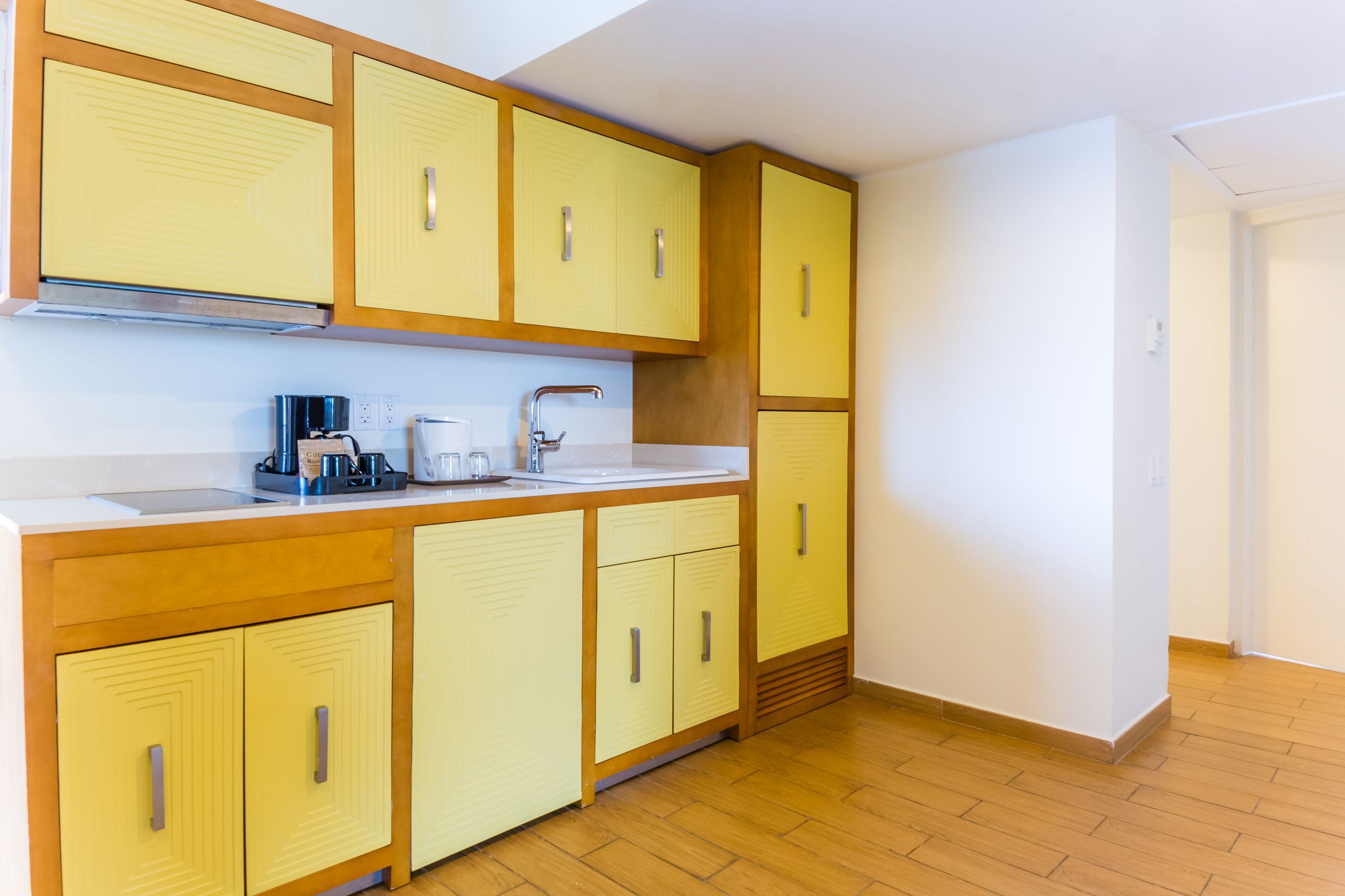 A kitchen with yellow cabinets, a white countertop, and a stainless steel sink.