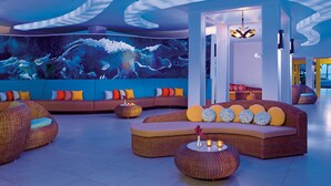 A modern lounge area with wicker furniture, a large wall mural, and a unique ceiling design.