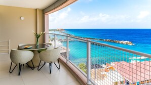 A balcony with a table and chairs, overlooking a turquoise sea and rocky coastline.