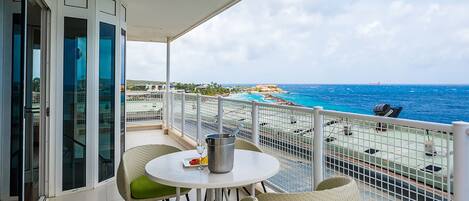 Un balcón con una mesa blanca y sillas de mimbre, con vista a la playa y al océano.