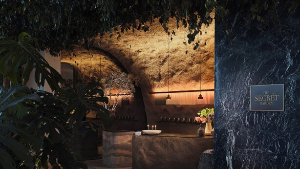 A dimly lit interior with a stone wall, a sign reading 'The Secret Garden,' and a wooden bench. - Hilton Athens (Athens)