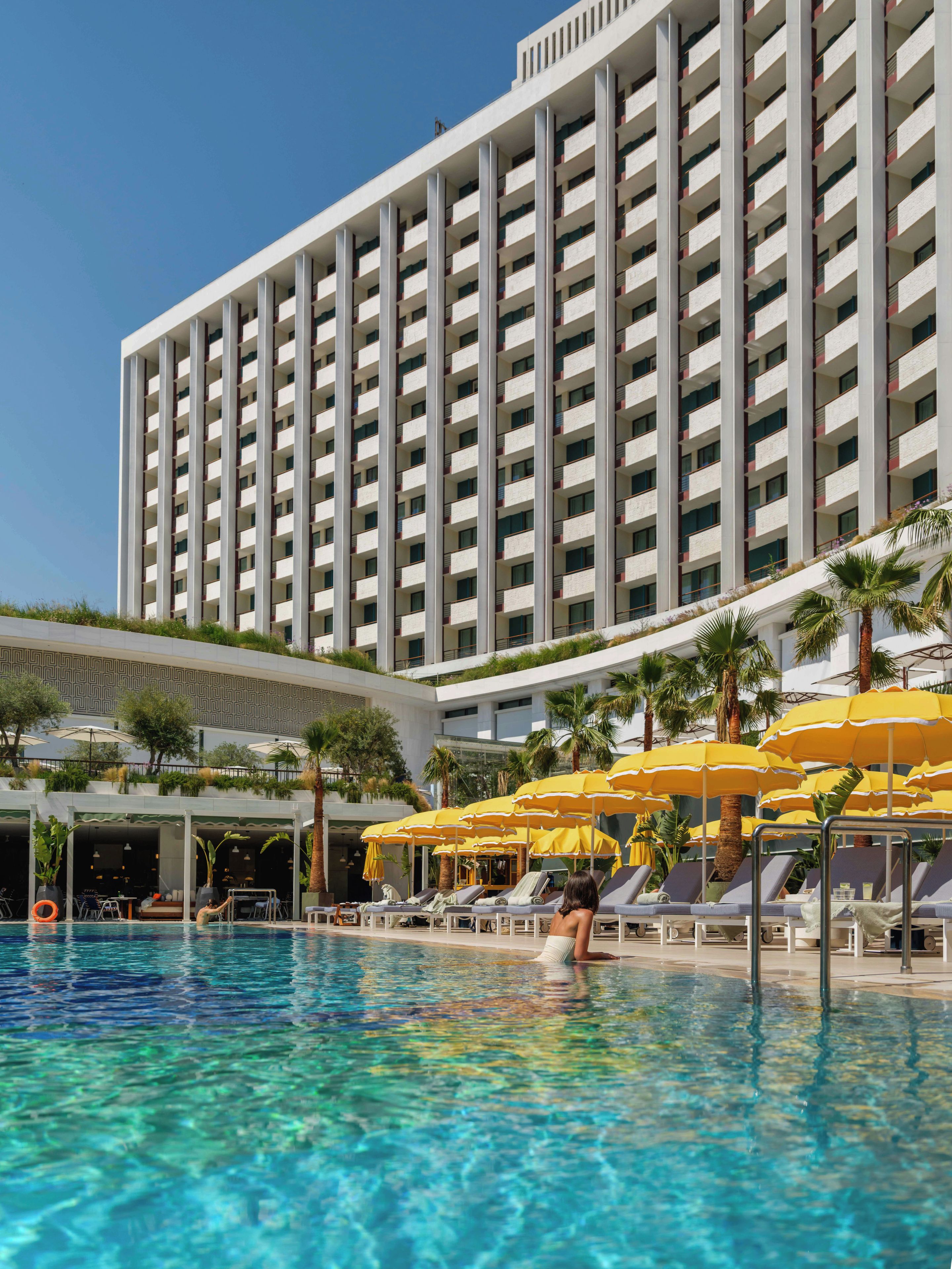 A hotel with a swimming pool, sun loungers, and umbrellas.