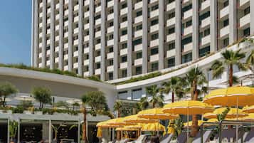 A hotel with a swimming pool, sun loungers, and umbrellas.
