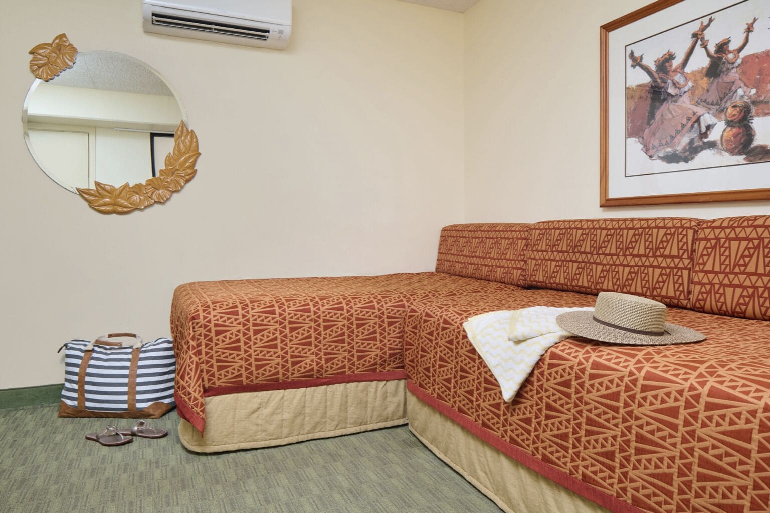 A hotel room with a bed, a mirror, a framed picture, a suitcase, and a hat.
