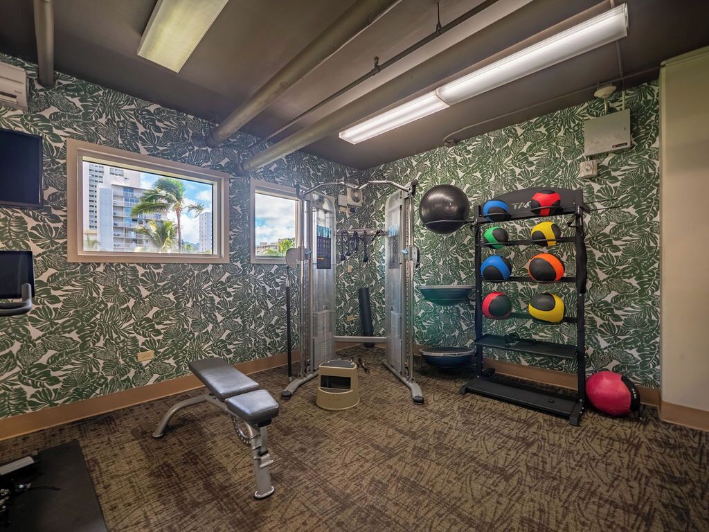 A gym with a weightlifting area, a bench, and a wall-mounted TV.