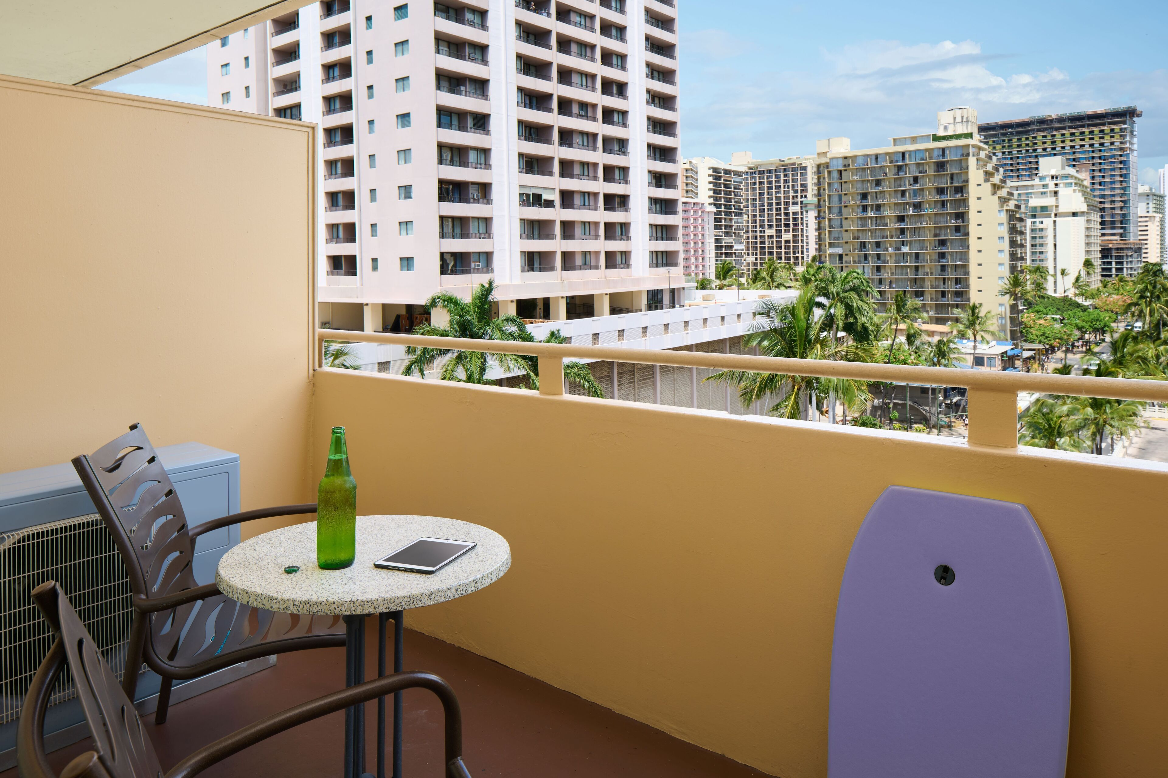 Un balcon avec une table, des chaises et une vue sur de hauts immeubles et des palmiers.