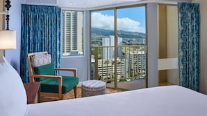 A hotel room with a large bed, a green chair, a small ottoman, and a view of a cityscape through a large window.
