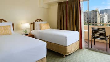 A hotel room with two beds, a balcony with a chair, and a view of city buildings.