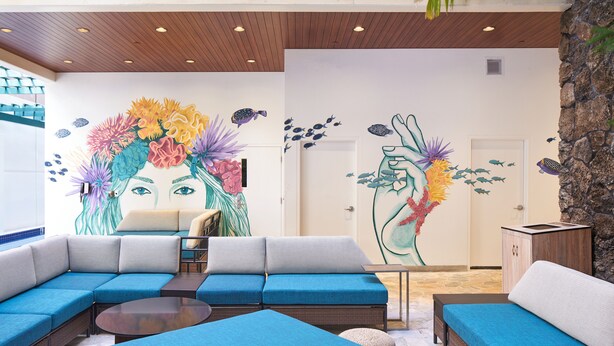 A modern lounge area with a large sectional sofa, a round coffee table, and a wall mural depicting a floral design.