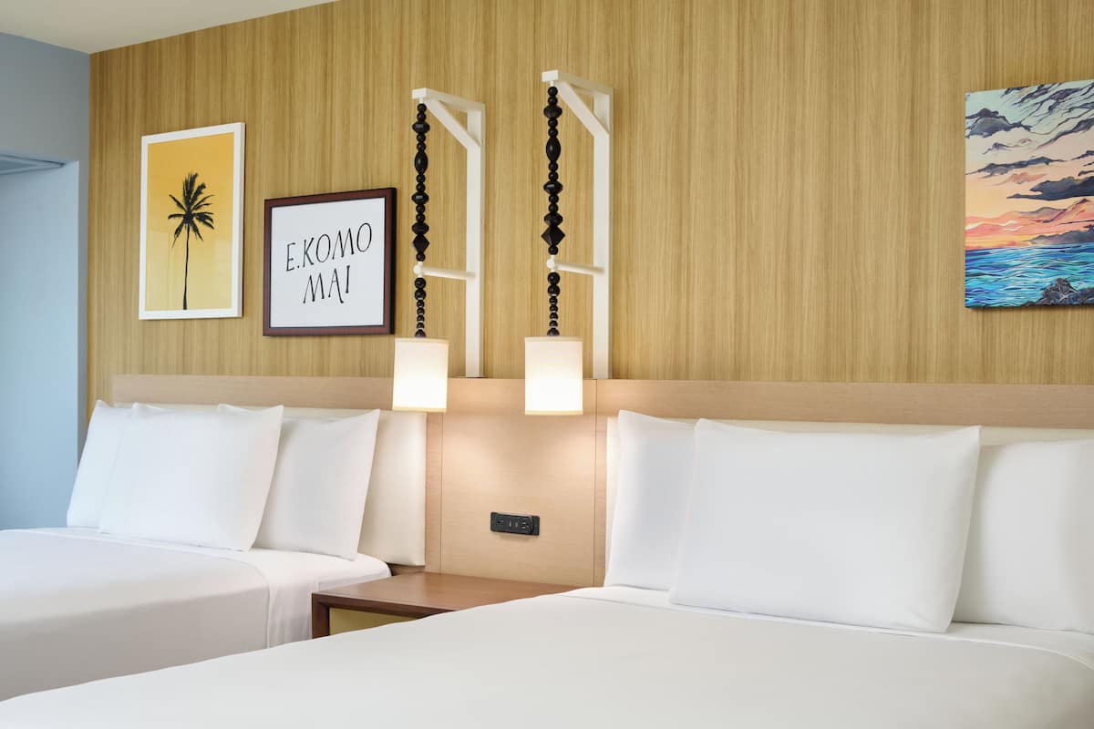 A hotel room with two beds, a wooden headboard, wall-mounted artwork, and a nightstand.