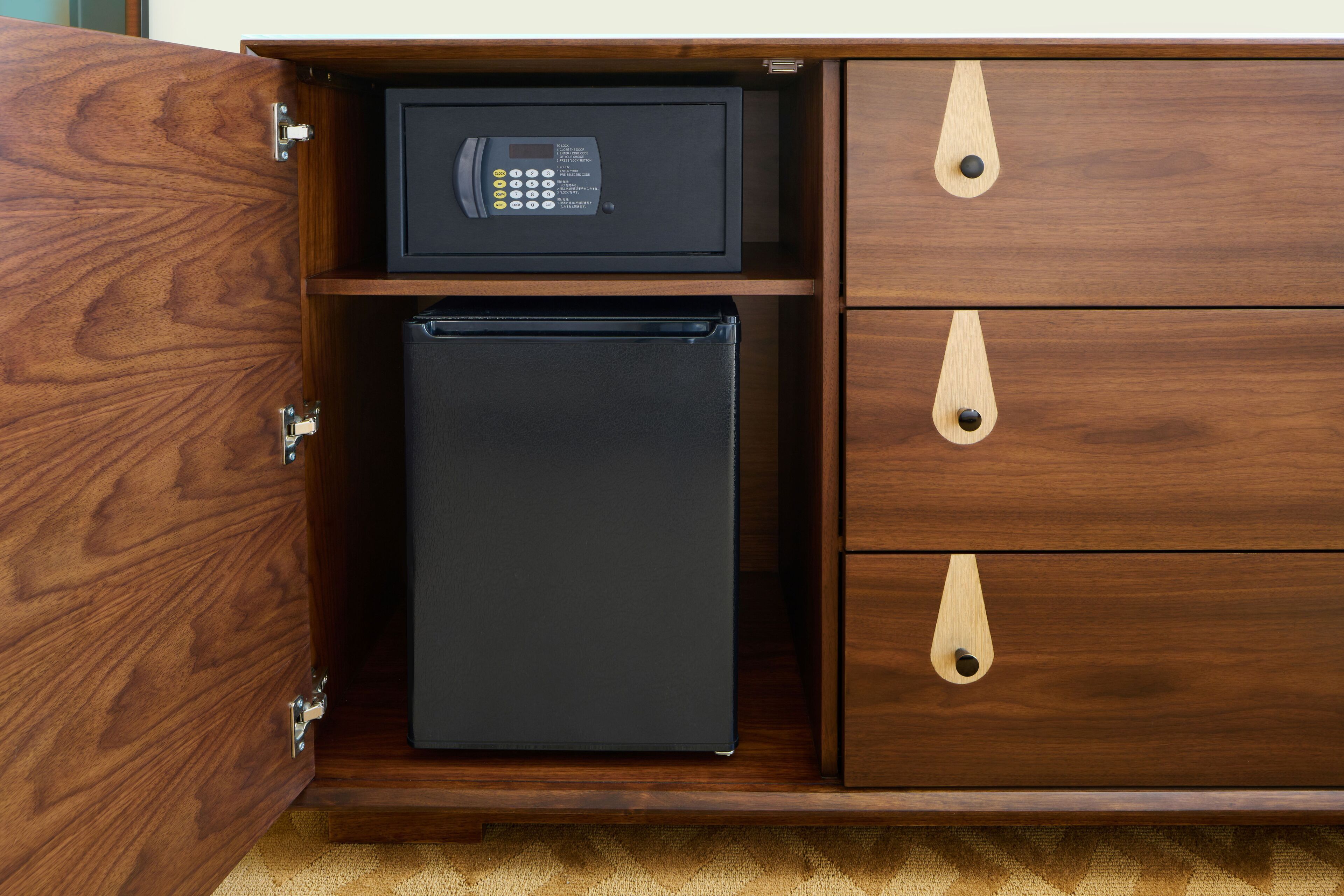 A wooden cabinet with a black safe and a black refrigerator.